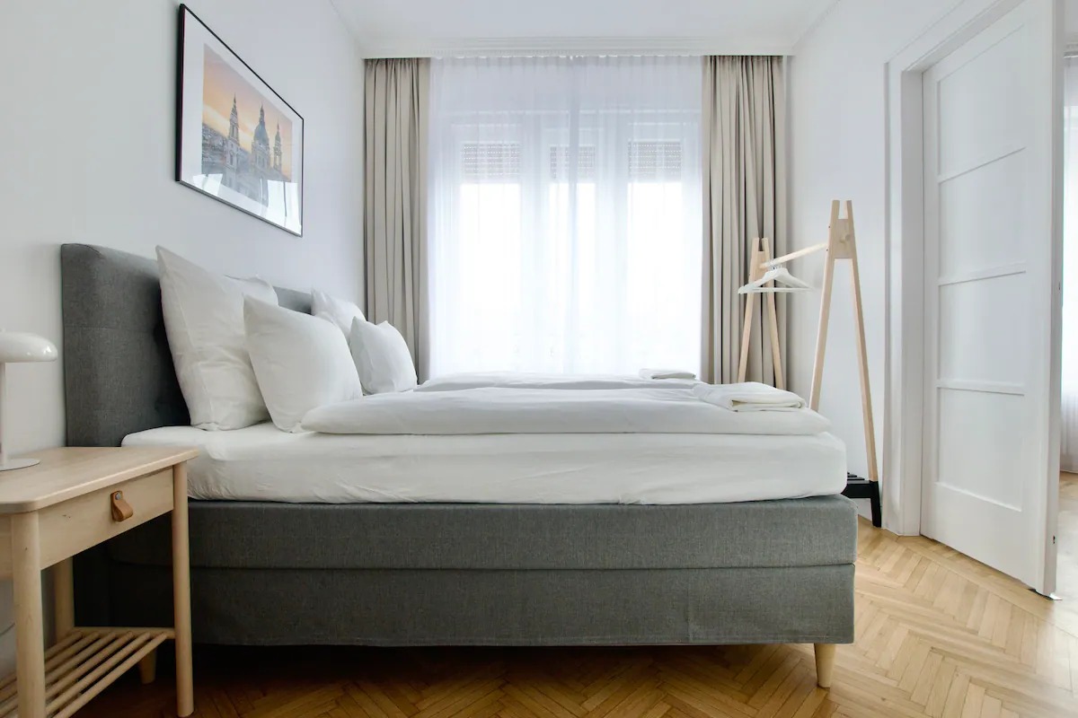 Padlótól mennyezetig érő bézs sötétítő és fehér fényáteresztő függöny egy modern hálószobában.